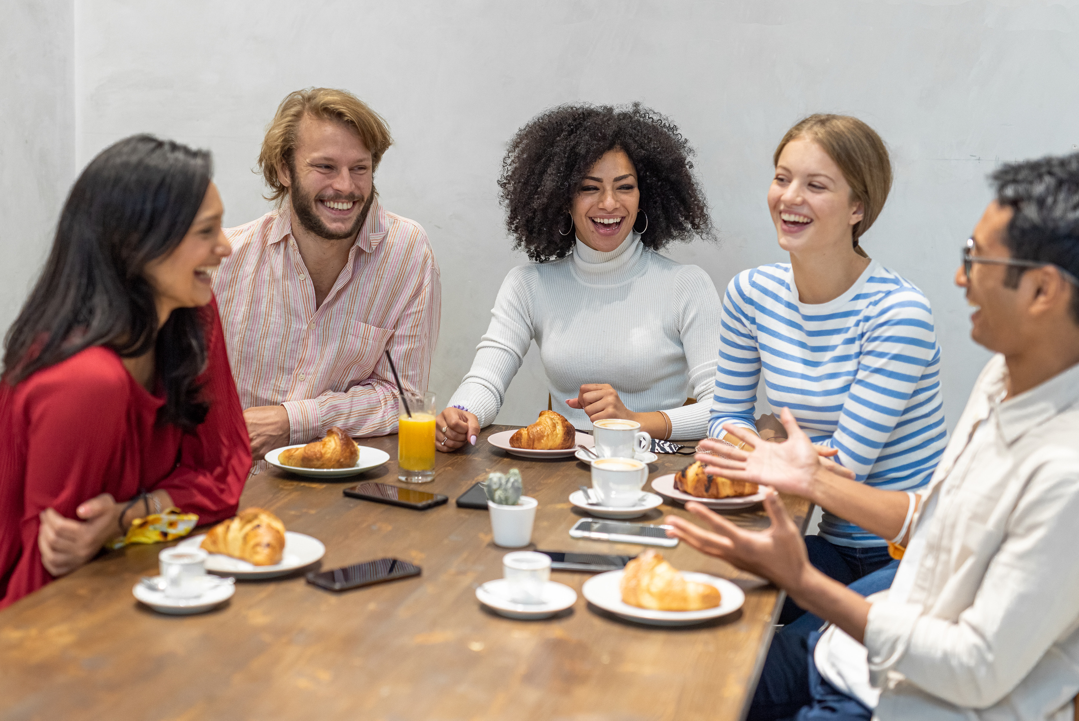 group of young millennials having breakfast, team work in a moment of pause, croissants and cakes, coffee and cappuccino on the table of a bar